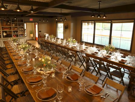 A banquet room with a long table set for a dinner party, filled with chairs, candles, flowers, and glassware.