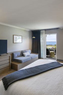 Bright living room with TV on stand, sofa, fireplace, and a seaside view through open sliding doors.