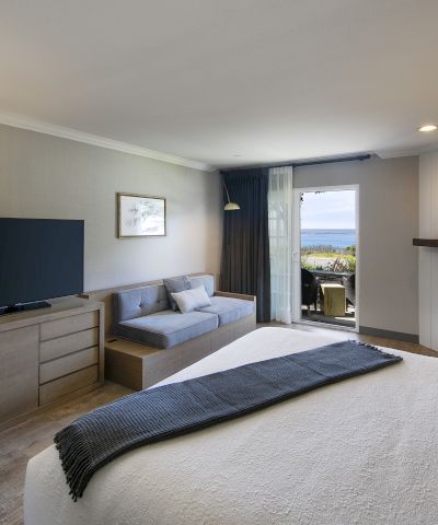 Bright living room with TV on stand, sofa, fireplace, and a seaside view through open sliding doors.