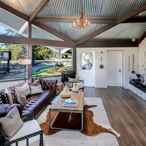 A modern living room with large windows, leather sofas, a coffee table, and a stone fireplace under a chandelier.