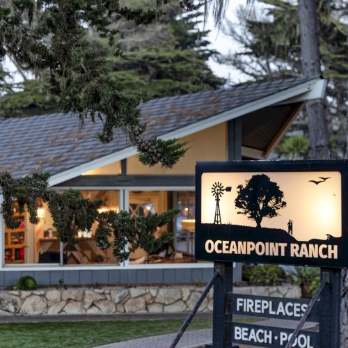 A sign for &ldquo;Ocean Point Ranch&rdquo; sits in front of a lodge, with greenery and tall trees framing the scene.