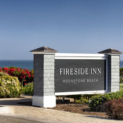 A Fireside Inn sign at Moonstone Beach with ocean and colorful flowers in the background.